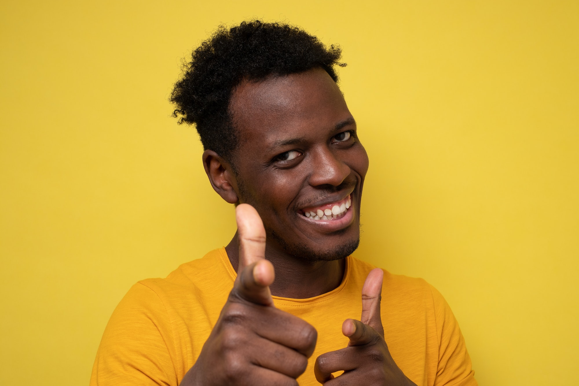 Funny young african man smiling happily and pointing his index fingers at camera